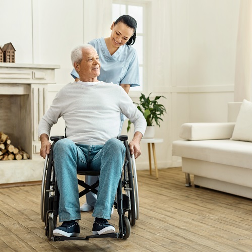 Medical professional smiling and standing behind elderly man smiling in wheelchair.
